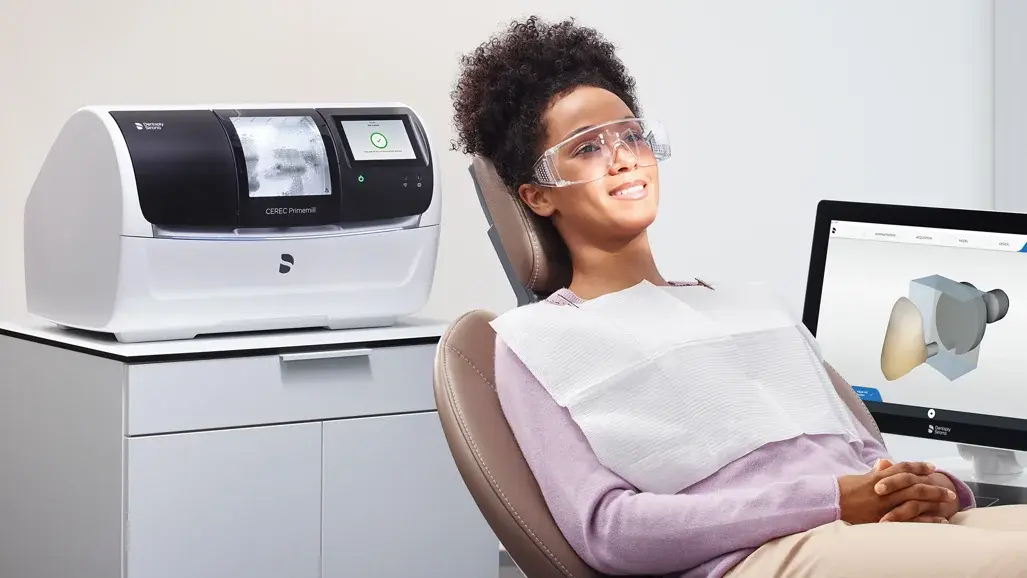 Smiling patient beside CEREC dental milling technology used to create custom ceramic restorations