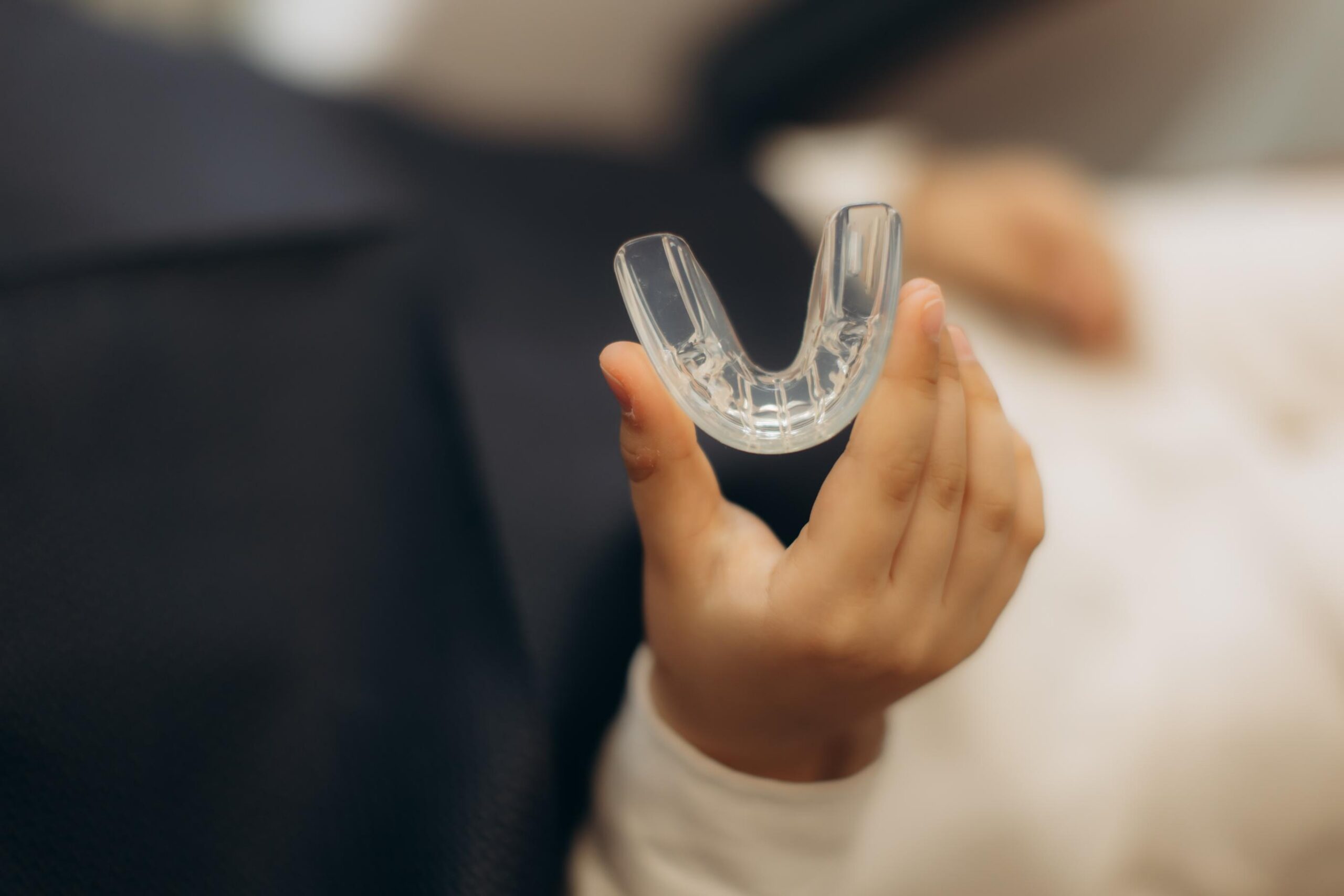 A child's hand holding a transparent dental retainer, illustrating removable orthodontic appliances and dental care