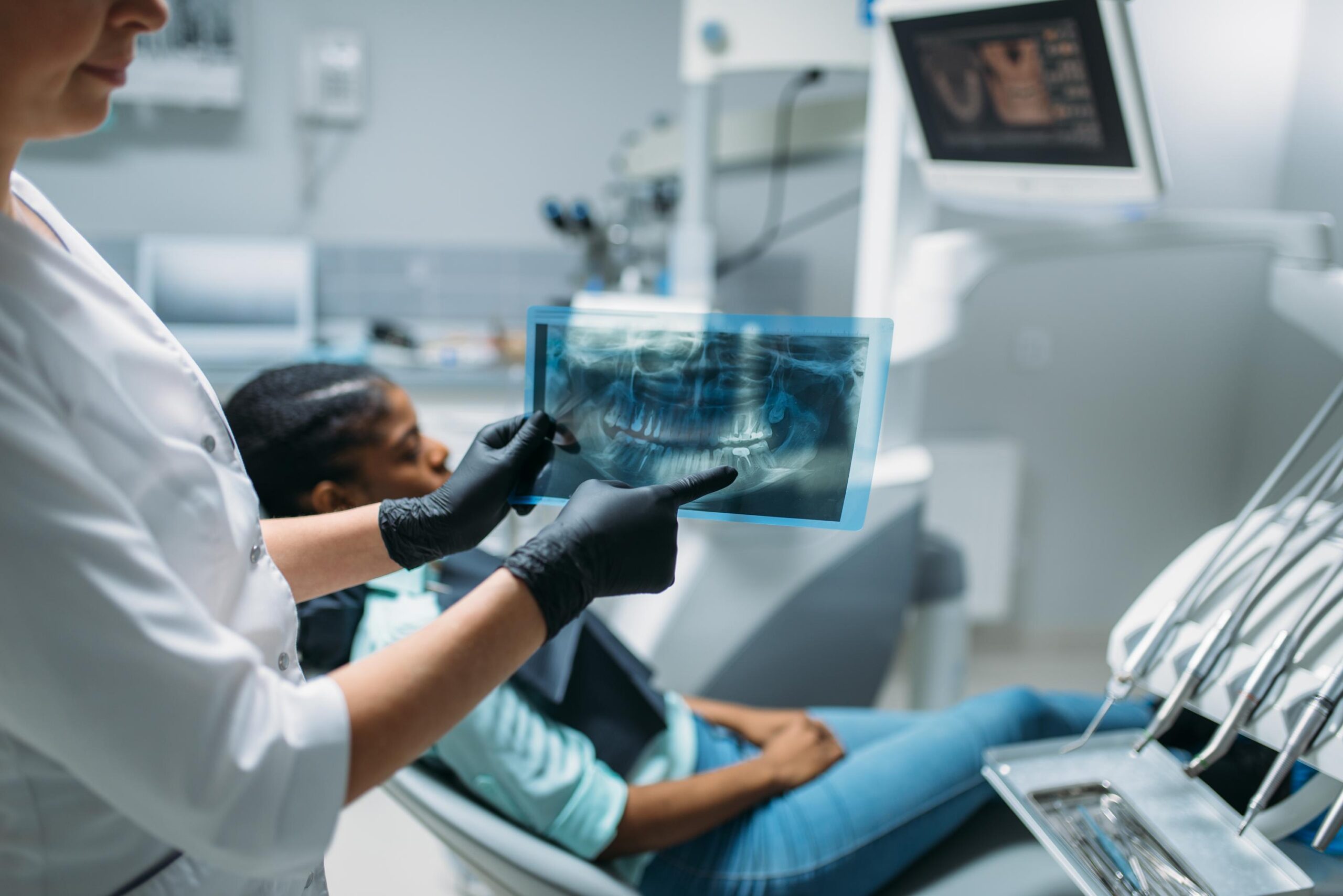 Patient reclining in a dental chair during a consultation with a dentist reviewing digital imaging