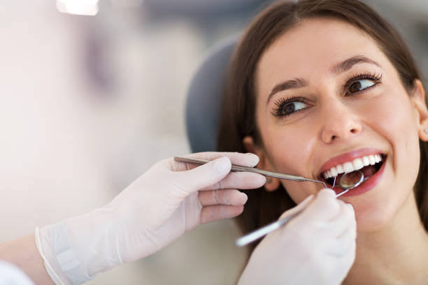 Woman receiving a dental examination while a dental professional checks her teeth with a handheld instrument
