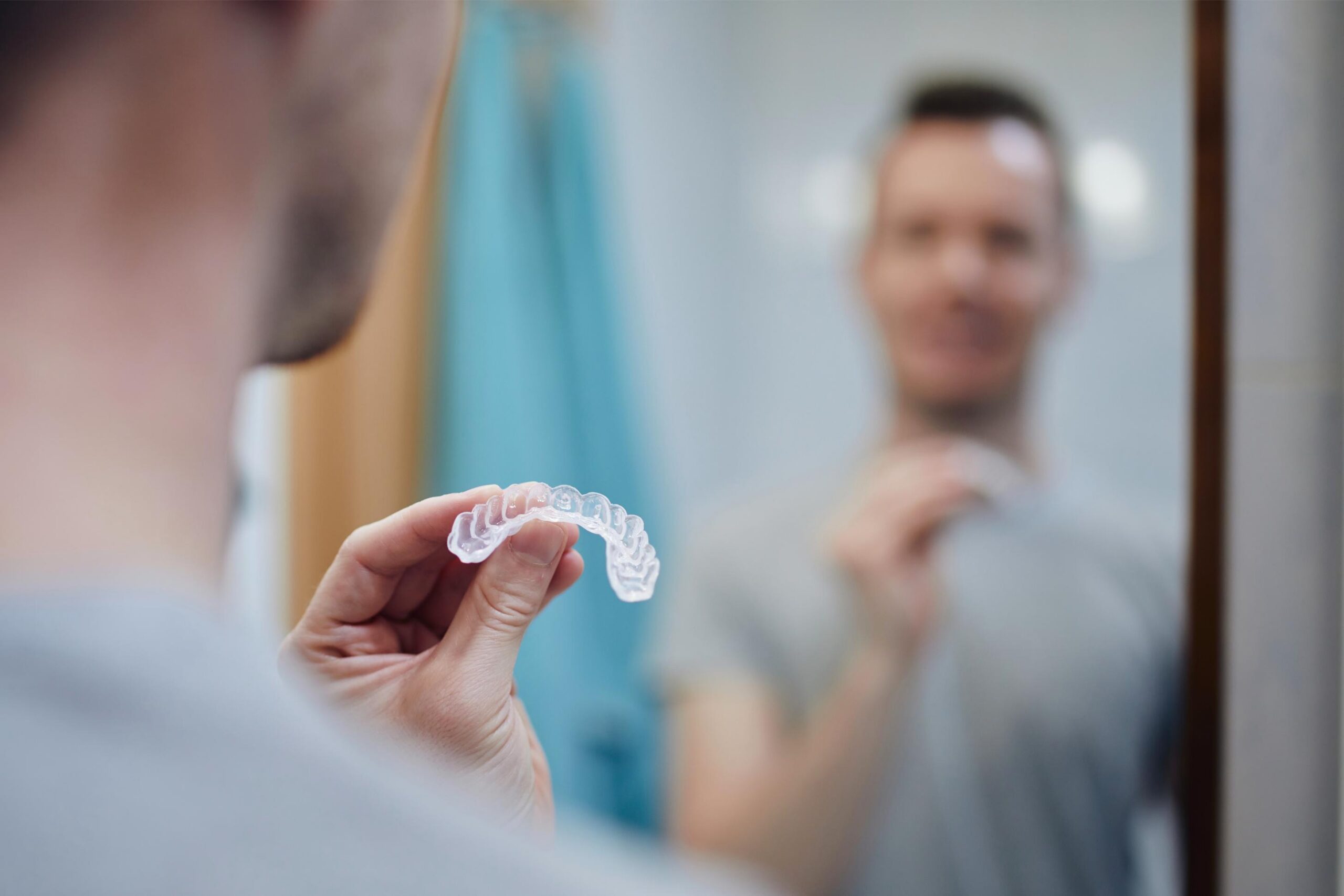Man examining a clear dental retainer while standing in front of a mirror