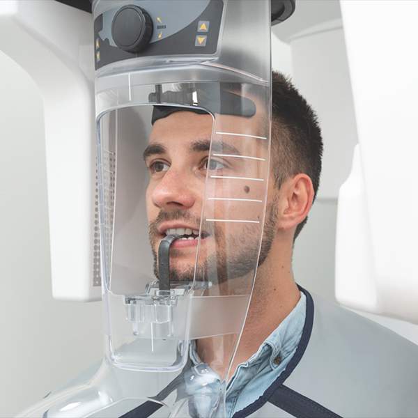 Smiling man positioned beneath digital dental imaging equipment during a diagnostic examination