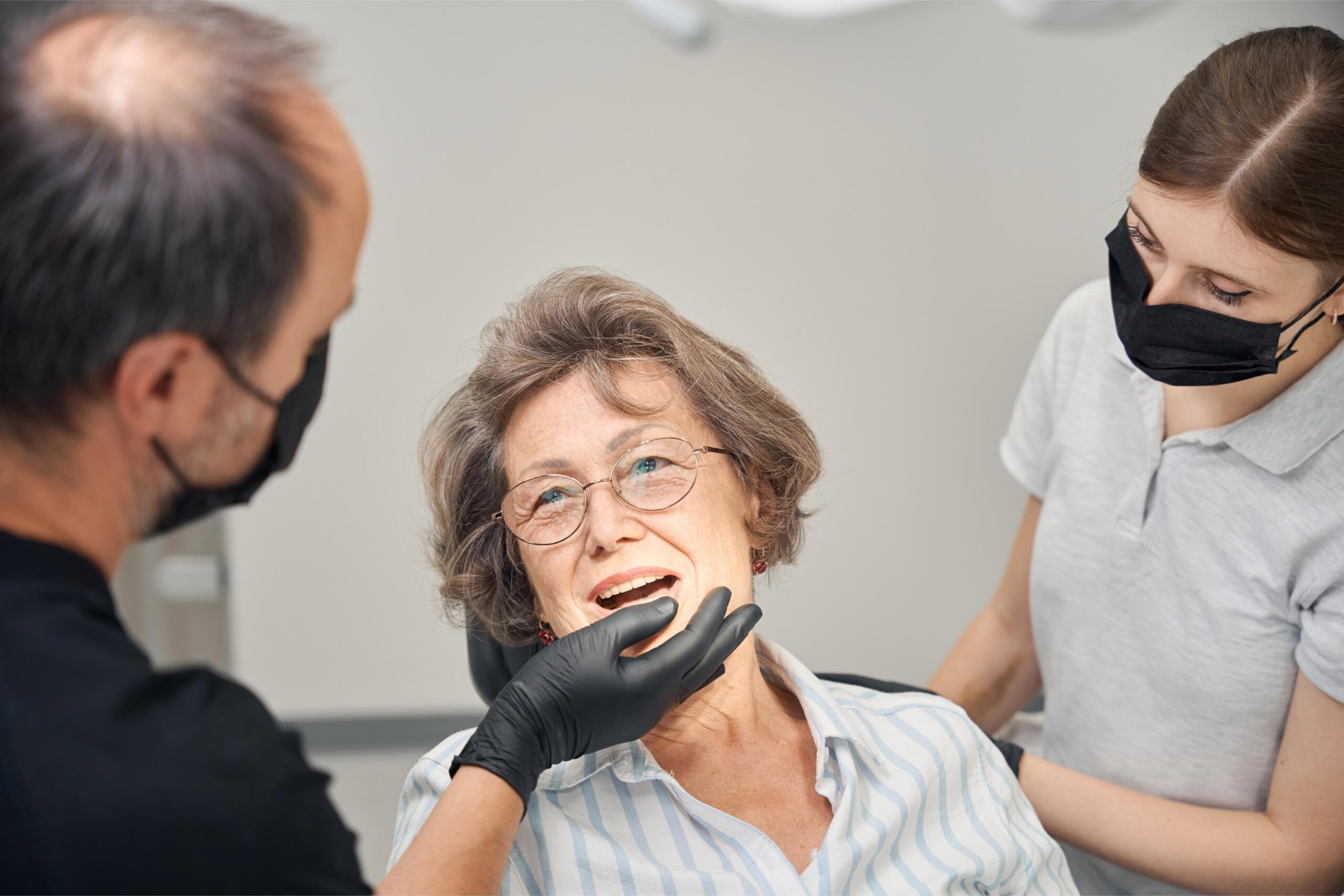 Older woman reclining in a dental chair while receiving attention from a dental professional
