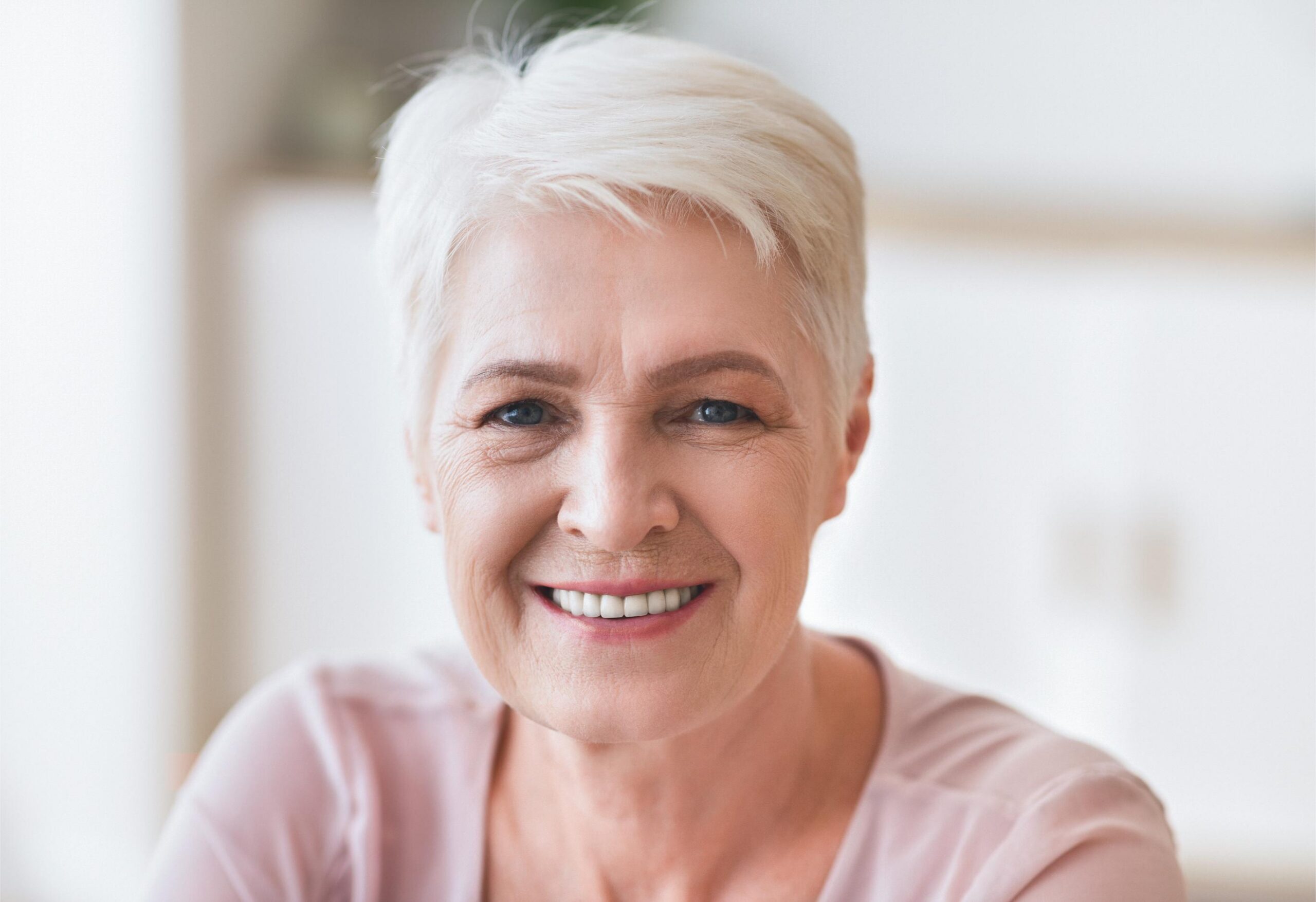 Older woman with short white hair smiling, representing natural-looking smiles and healthy aging