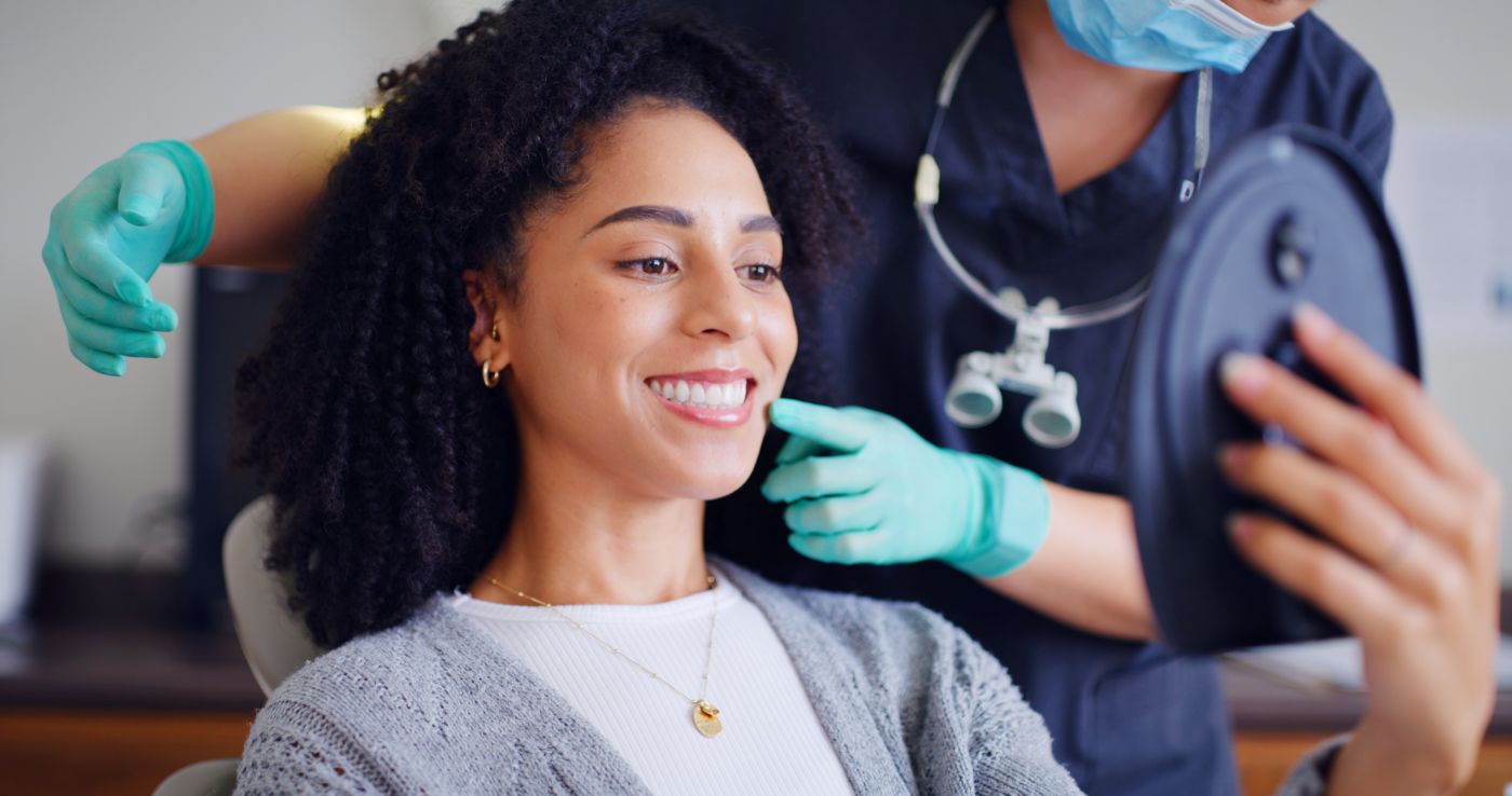 Smiling woman receiving dental care while holding a mirror to see her reflection