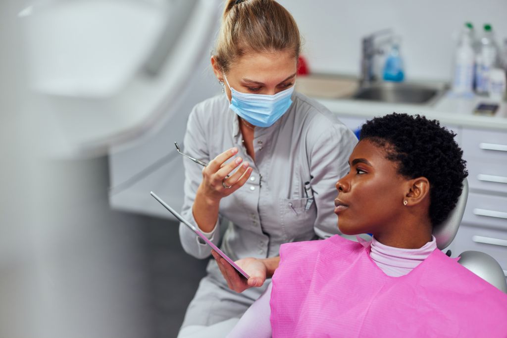 Dentist wearing a surgical mask explaining a dental procedure to a patient in the treatment chair