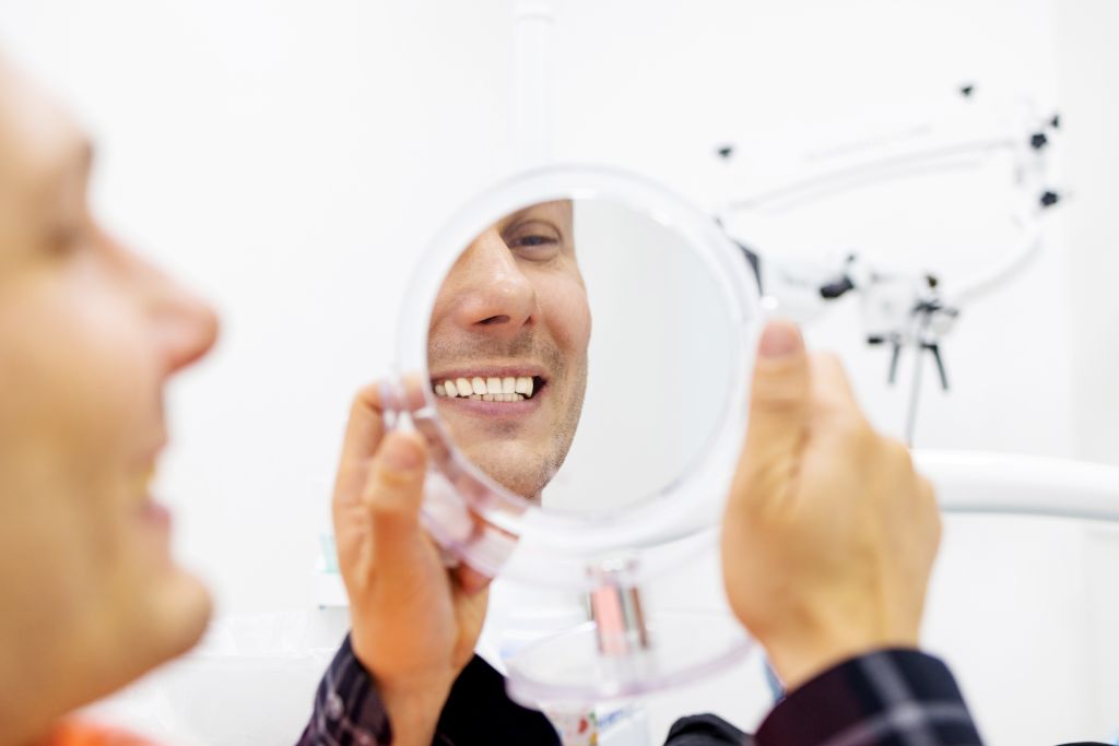 Smiling man holding a mirror while examining his teeth following a cosmetic dental consultation