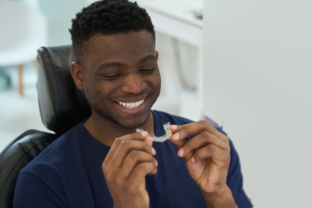 Smiling young man looking downward, while he holds his clear aligners close to his face