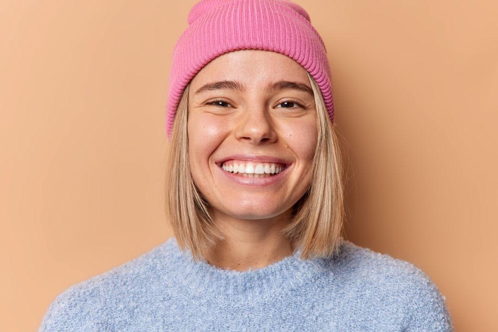 Smiling woman wearing a pink knit hat, showcasing a healthy and confident smile